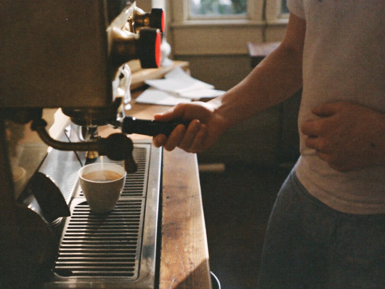 The counter at 7am — a barista's hands mid-tamp, 35mm film